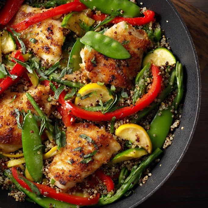 A colorful plate featuring flaky fish, golden quinoa, and a vibrant mix of green and purple vegetables, drizzled with a zesty lemon herb sauce.
